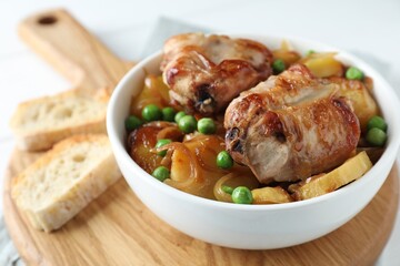 Tasty cooked rabbit with vegetables in bowl and bread on wooden board, closeup