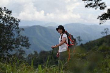 An Asian woman with a backpack and trekking pole standing and enjoying the fresh air while hiking...