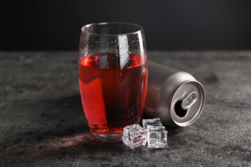 Energy drink in glass, aluminium can and ice cubes on grey table, closeup