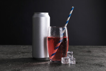 Energy drink in glass, aluminium can and ice cubes on grey table
