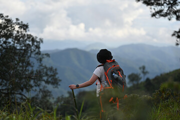 Rear view of an Asian woman with a backpack and trekking pole standing and enjoying the fresh air...