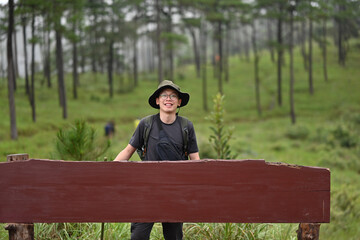 Fototapeta premium Young Asian adventurer with a backpack posing with a blank sign, the concept of conquering the trail and nature tourism