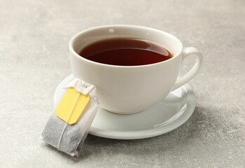 Tea bag and cup of aromatic drink on grey textured table, closeup