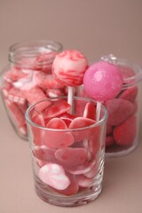 Obraz na płótnie Canvas Tasty pink candies in glass jars on light brown background, closeup