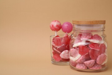 Tasty pink candies in glass jars on beige background, space for text