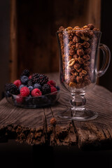 Chocolate granola in a glass. Colorful berries in the background. Breakfast with granola and berries.