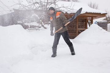 A man in work clothes removes snow in the yard of his house. Snow dust flies in the air.