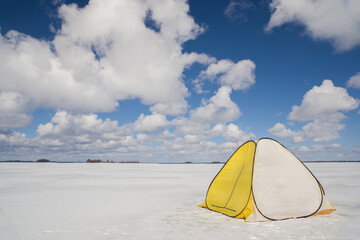 A fishing tent stands on the ice of a lake.