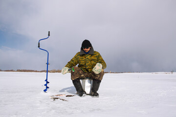 A man fisherman catches fish on the ice of a frozen lake.