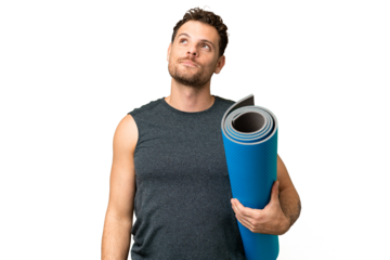 Young sport man going to yoga classes while holding a mat over isolated chroma key background thinking an idea while looking up