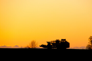 Fototapeta premium Sugar beet lifts in golden sunset in silhouette