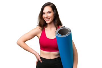 Young sport woman going to yoga classes while holding a mat over isolated background posing with arms at hip and smiling