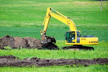 An excavator while digging a trench in a green field
