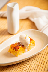 Torrija con bola de helado artesano de vainilla con caldo de vainilla templado sobre plato blanco en un restaurante gourmet