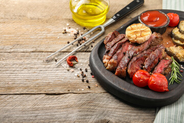 Delicious grilled beef with vegetables and spices on wooden table, space for text