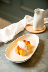 Torrija con bola de helado artesano de vainilla bañado con caldo de vainilla templada en vajilla blanca sobre una mesa de restaurante goumet