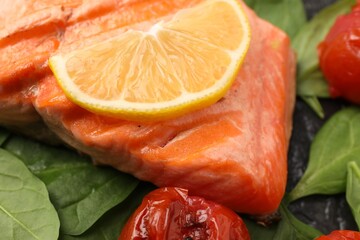 Tasty grilled salmon with lemon, spinach and tomatoes on table, closeup
