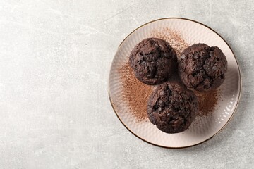 Delicious chocolate muffins and cacao powder on light grey table, top view. Space for text