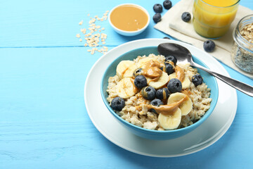 Tasty oatmeal with banana, blueberries and peanut butter served in bowl on light blue wooden table, space for text