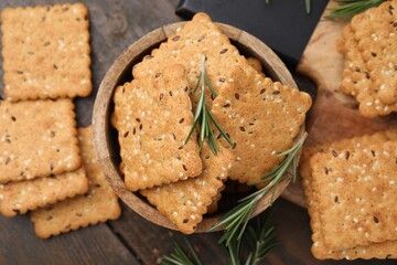 Cereal crackers with flax, sesame seeds and rosemary on wooden table, flat lay