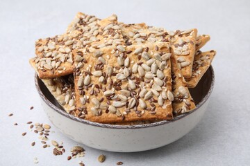 Cereal crackers with flax, sunflower and sesame seeds in bowl on light textured table, closeup