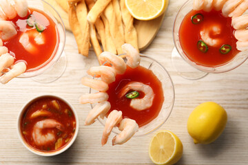 Tasty shrimp cocktail with sauce in glasses and lemon on light wooden table, flat lay