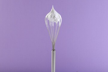 Whisk with whipped cream on violet background