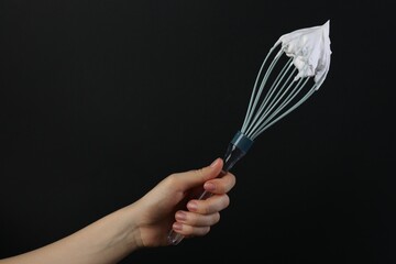 Woman holding whisk with whipped cream on black background, closeup. Space for text
