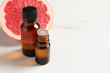 Grapefruit essential oil in bottles and fruit on white table, closeup. Space for text