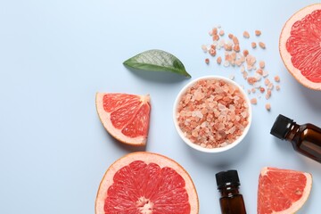 Grapefruit essential oil in bottles, sea salt and cut fruit on light blue table, flat lay. Space for text