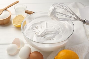 Bowl with whipped cream, whisk and ingredients on white wooden table