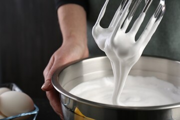 Woman making whipped cream with hand mixer on black background, closeup