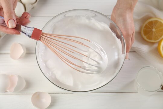 Woman making whipped cream with whisk at white wooden table, above view