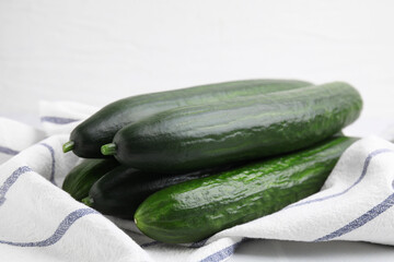 Fresh cucumbers and cloth on white table, closeup