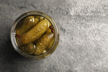 Tasty pickled cucumbers in glass jar on grey table, top view. Space for text