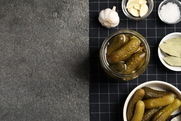 Tasty pickled cucumbers and spices on grey textured table, top view. Space for text