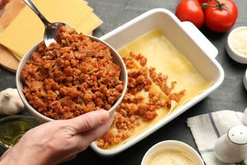 Woman making lasagna at dark table, closeup