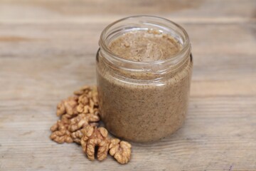 Tasty nut paste in jar and walnuts on wooden table, closeup