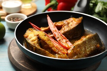 Tasty fish curry in frying pan and ingredients on light blue wooden table, closeup. Indian cuisine