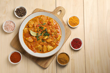 Delicious chicken curry and spices on wooden table, flat lay. Space for text