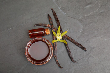 Aromatic vanilla extract, pods and flower on black table, flat lay
