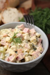 Tasty Olivier salad with boiled sausage in bowl on table, closeup