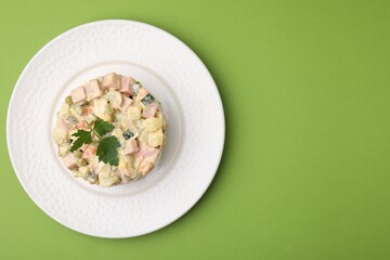 Tasty Olivier salad with boiled sausage on green table, top view. Space for text
