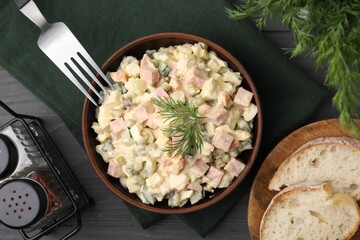 Tasty Olivier salad with boiled sausage in bowl served on grey wooden table, flat lay