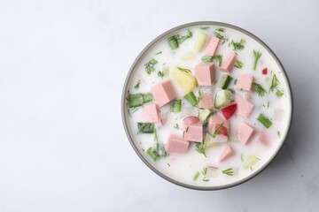 Delicious cold summer soup (okroshka) with boiled sausage in bowl on white table, top view. Space for text