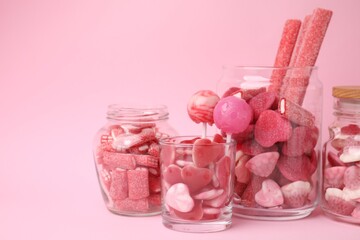Tasty candies in glass jars on pink background, space for text