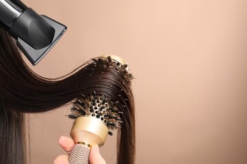 Hairdresser blow drying client's hair on beige background, closeup. Space for text © New Africa