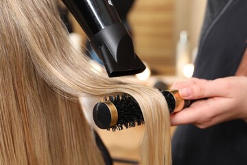 Naklejka premium Hairdresser blow drying client's hair in salon, closeup