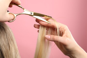 Hairdresser cutting client's hair with scissors on pink background, closeup