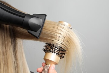 Hairdresser blow drying client's hair on light grey background, closeup